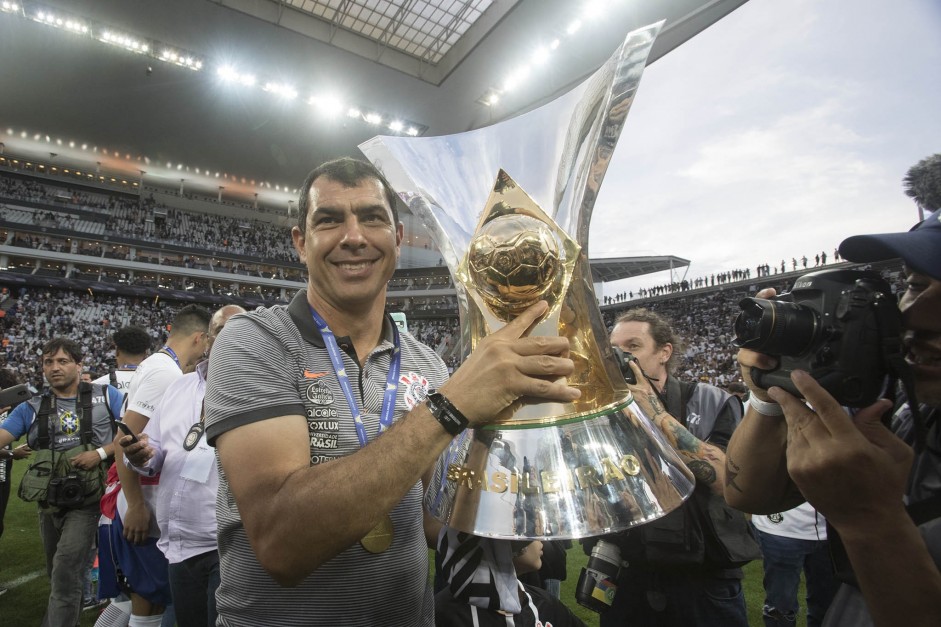 Carille posa com taça de campeão brasileiro na Arena Corinthians; treinador está de volta